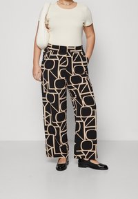 Pantalones de pierna ancha negros con un patrón geométrico beige, combinados con una blusa ligera de canalé y zapatos planos negros. Los accesorios incluyen un bolso blanco.
