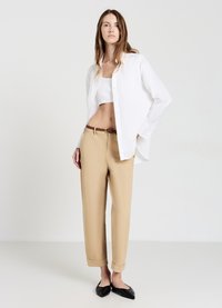 Camicia bianca button-up, top bianco corto, pantaloni beige con risvolti, cintura intrecciata marrone e scarpe nere eleganti a punta.