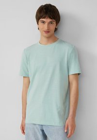 Lichtblauw katoenen T-shirt met korte mouwen en een ronde hals. Heeft een zachte textuur en een relaxte pasvorm. Draagt bij lichte denim jeans.