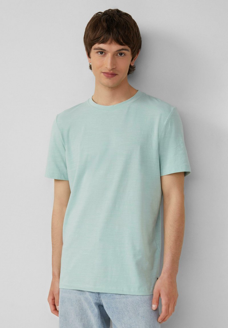 Lichtblauw katoenen T-shirt met korte mouwen en een ronde hals. Heeft een zachte textuur en een relaxte pasvorm. Draagt bij lichte denim jeans.