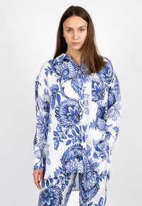 Floral-patterned button-up shirt in blue and white, made of lightweight fabric. Features a collar and pockets, with long sleeves.