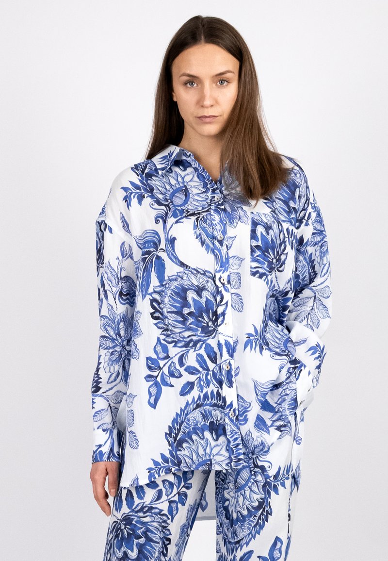 Floral-patterned button-up shirt in blue and white, made of lightweight fabric. Features a collar and pockets, with long sleeves.