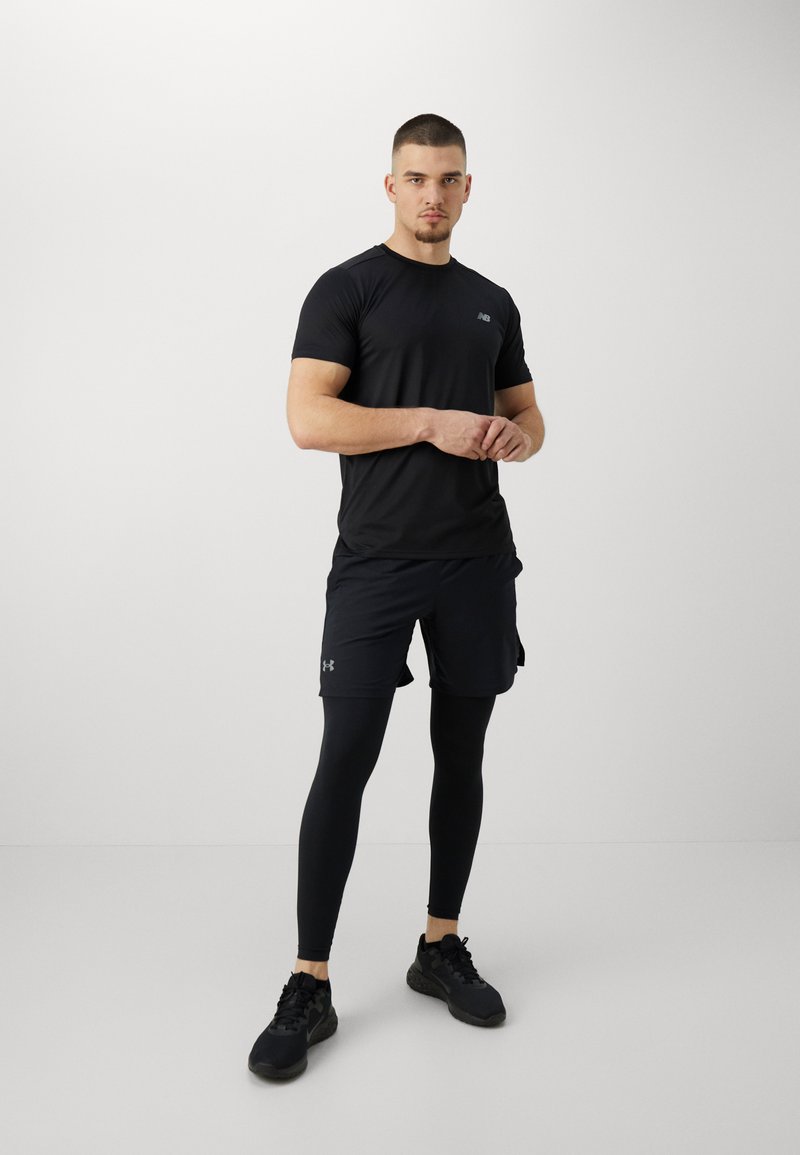 T-shirt de sport noir, design ajusté, manches courtes. Assorti avec un short noir, superposé avec un legging noir. Des baskets noires complètent le look.