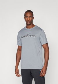 Grå Nike Pro T-skjorte, kortermet, rund hals. Har en svart Nike Pro-logo over brystet, myk stoff med en jevn tekstur.