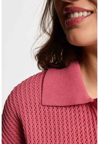 Roze gebreide polo met een geribde kraag en kleine ruitpatronen. De stof heeft een gestructureerde, ademende uitstraling.