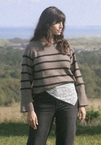 Pull rayé marron avec une coupe décontractée, associé à un jean noir et une dentelle blanche à la taille. Texture douce, manches larges.