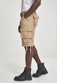 Khaki cargo shorts, joissa on useita taskuja, säädettävät nyörit ja rento istuvuus, yhdistettynä mustiin nauhakenkiin.