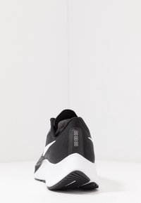 Chaussure de sport noire avec une tige texturée, des accents blancs et une semelle épurée. Dispose d'un affichage numérique sur le talon pour suivre la performance.