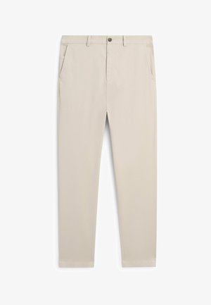 Beige, nauwsluitende broek met steekzakken aan de voorkant, lussen voor een riem en een knoopsluiting, plat liggend op een witte achtergrond.