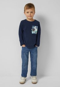 Granatowa koszulka z długim rękawem z nadrukiem na kieszeni, zestawiona z niebieskimi dżinsami i jasnymi trampkami. Prosty, codzienny styl.