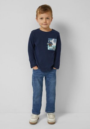 Marineblaues Langarm-T-Shirt mit einem grafischen Taschenprint, kombiniert mit blauen Jeans und hellen Sneakern. Einfaches, legeres Design.