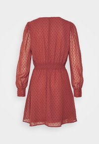 Rotes Kleid aus durchsichtigen Stoff mit Punktemuster, langen Ärmeln, elastischem Bund und Knopfmanschetten. Der Saum ist über dem Knie.