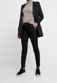 Pantalon noir ajusté, pull à col roulé beige et blazer foncé. Baskets noires avec semelle blanche. Tissus lisses et design sur mesure.
