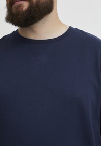 Maglione girocollo in cotone blu navy con colletto a coste e un piccolo dettaglio a V nella scollatura. Tessuto morbido, vestibilità casual.