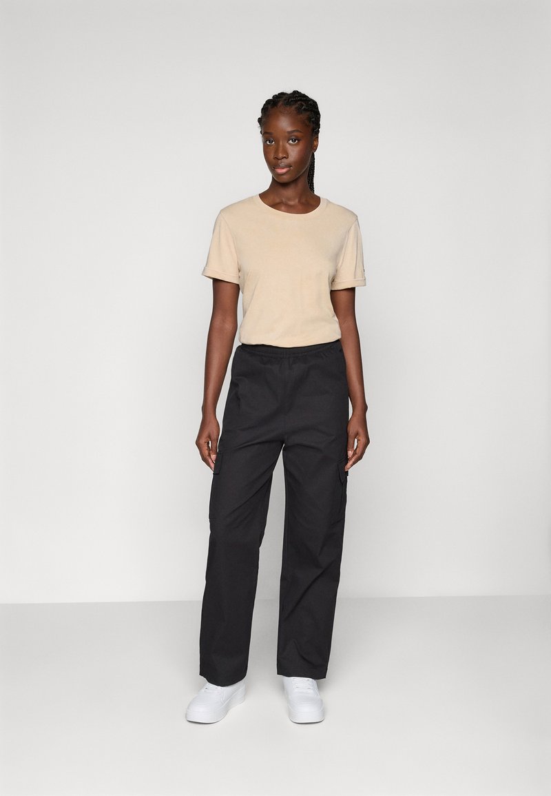 T-shirt beige a maniche corte e pantaloni cargo neri con vita elastica. Sneakers bianche. Texture liscia, vestibilità comoda, tasche laterali sui pantaloni.