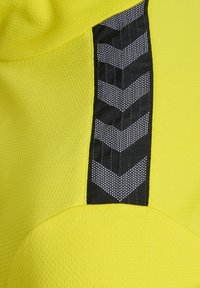 Gelbes Sportmaterial mit strukturierten Oberflächen, das ein vertikales schwarzes Panel mit reflektierenden Chevron-Mustern und Nähtdetails aufweist.