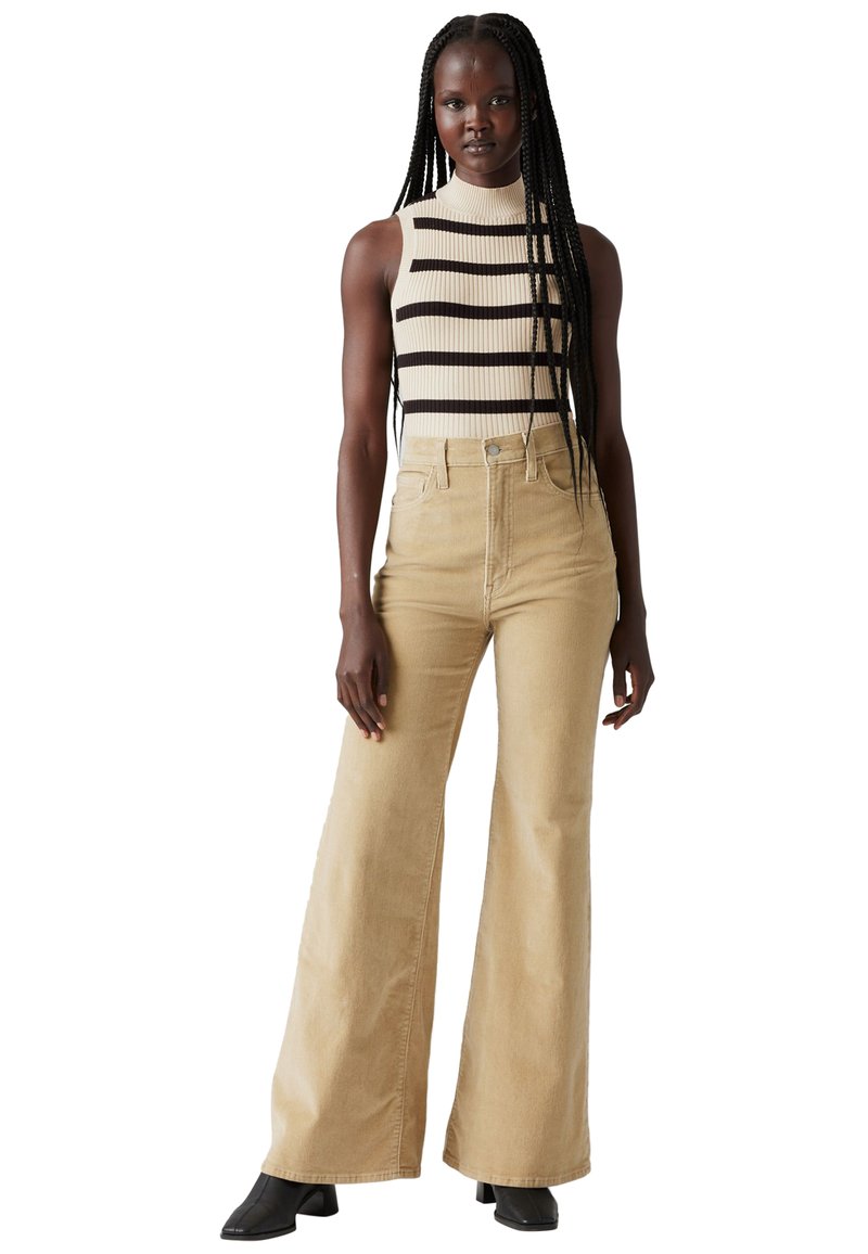 Un bonnet à rayures en crème et marron foncé, associé à un pantalon beige taille haute et à jambes larges. Tissu texturé, design minimaliste.