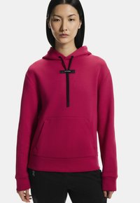 Fuchsiová mikina so prednou vreckom, s kapucňou na šnúrku a čiernymi akcentmi. Materiál má hladkú textúru a voľný strih.