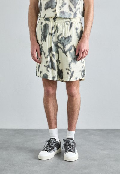 Shorts crème légers avec un motif abstrait noir et gris, taille élastique, assortis à des baskets grises et des chaussettes blanches.
