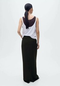 Witte tanktop gelaagd over een bruine top, gedragen met een fitted olijfgroene maxi rok met een split aan de achterkant en een soepele textuur.