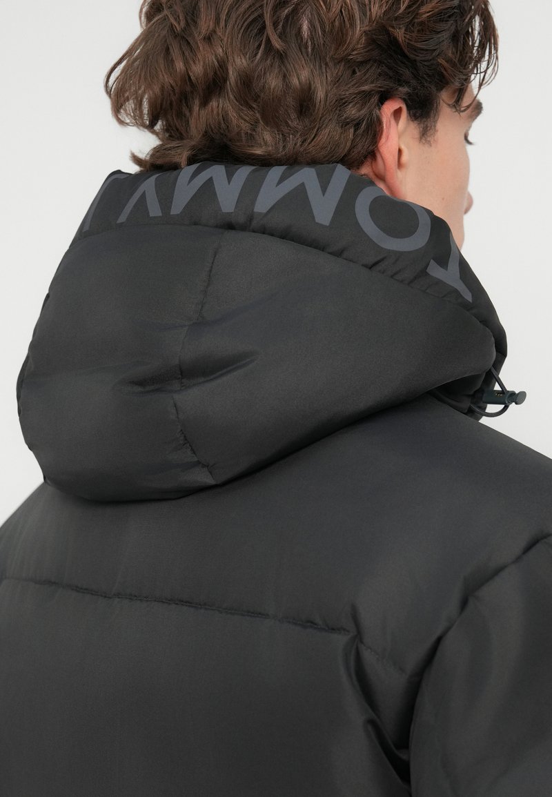 Schwarze gepolsterte Jacke mit Kapuze und Kordelzug. Verfügt über ein Logo auf der Rückseite des Kragens, eine glatte Textur und ein schlankes Design.