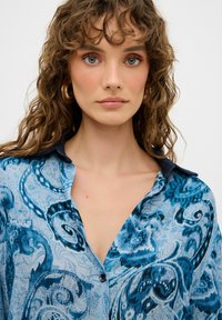 Camicia a fantasia blu con vortici in diverse tonalità di blu, dotata di colletto e chiusura con bottoni, realizzata in un tessuto leggero.