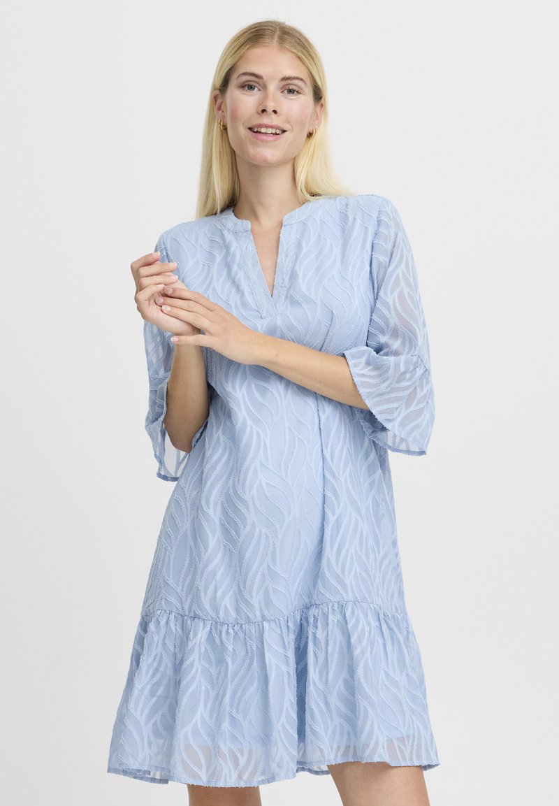 Rochie bleu deschis cu decolteu în V, mâneci trei sferturi și tiv cu volane stratificate. Fabricată dintr-un material texturat cu un model în valuri.