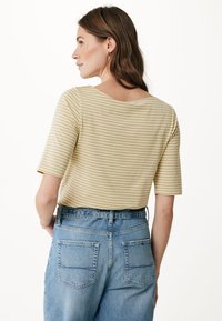 Pruhované žluté tričko s krátkými rukávy, kulatým výstřihem; v kombinaci s džíny z modrého denimu s vysokým pasem, které mají zadní kapsy a poutka na pásek.