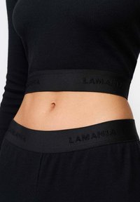 Must muströöpidega lühike topp koos sobiva vöökohtaga. Omab reljeefset "LAMANIA" logo, kinnist disaini ja sujuvat tekstuuri.