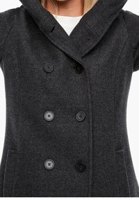 Cappotto di lana grigio scuro con design doppiopetto, ampio colletto e bottoni neri. Presenta tasche laterali e un tessuto testurizzato.