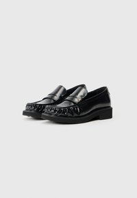 Mocassins de couro preto com bico arredondado, detalhes cosidos ao longo da borda e um salto baixo em bloco. Textura lisa e brilhante.