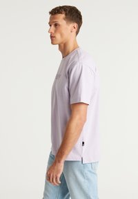 Šviesiai purpurinė medvilninė marškinė su trumpomis rankovėmis, apvalia iškirpte ir mažu siuvinėtu logotipu priekyje. Apatinėje dalyje yra šoninės plyšio.