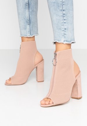 Brzoskwiniowe dziane botki za kostkę mają otwarty nosek, boczne wycięcia i tylny zamek, a także masywny obcas i prążkowany mankiet dla dodatkowego efektu.