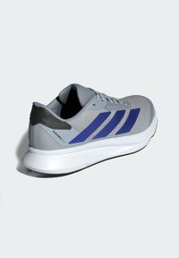 Gray athletic shoe with a mesh upper, featuring three blue stripes, a black heel accent, and a white sole. Textured material and sleek design.