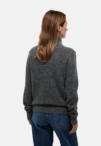 Pull gris texturé à col montant avec poignets et ourlet côtelés, associé à un jean bleu. Le tissu semble doux et légèrement duveteux.