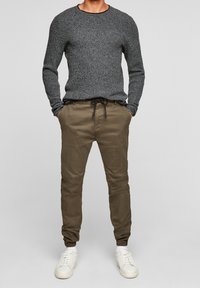 Pull gris en tricot avec col rond, associé à un pantalon fuselé vert olive avec une taille élastique. Baskets avec des accents blancs.