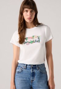 T-shirt en coton blanc avec un graphisme floral et le texte "Levis" en gras, associé à un jean taille haute en denim texturé.