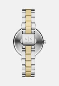 Kaksitooniline hõbe- ja kuldmetallist Armani Exchange'i kellarihm, mille lukul on graveering "A|X Armani Exchange", vaadatud tagantpoolt.