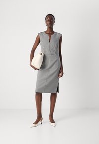 Robe à carreaux noir et blanc avec un décolleté en V profond, taille cintrée et fente sur le côté. Associée à un sac à main blanc et des escarpins à bout pointu.
