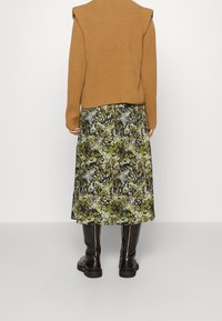 Pull en maille marron à épaules évasées, associé à une jupe midi florale dans des tons de vert et de noir. Bottes noires jusqu'aux genoux.