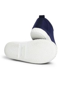 Zapatilla de lienzo azul marino con una suela de goma blanca texturizada. Las características incluyen una lengüeta en el talón y un diseño de cuerpo superior liso.
