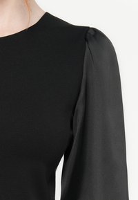 Black dress featuring a structured bodice with soft, flowing long sleeves. Smooth texture with subtle sheen on sleeves. Classic round neckline.