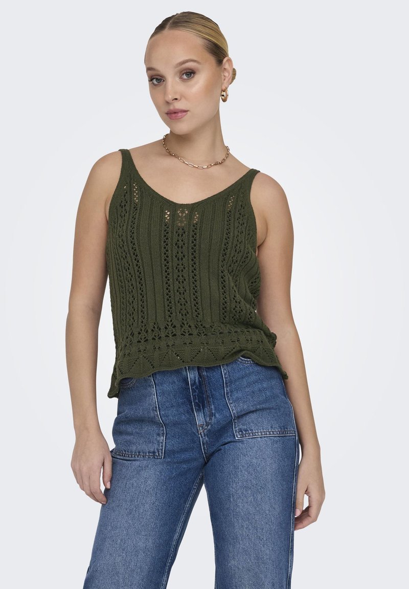 Top de punto verde oliva sin mangas con un dobladillo festoneado, que presenta patrones de calados y tirantes anchos. Combinado con unos vaqueros de mezclilla azul de cintura alta.