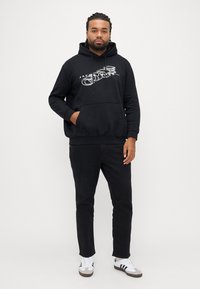 Černá mikina s kapucí a přední kapsou s grafickým potiskem. Kombinována s černými kalhotami a bílými teniskami s černými detaily.