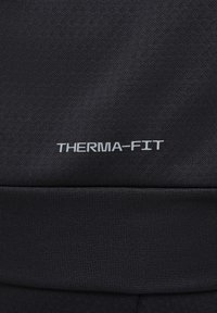 Zwarte stof met een gestructureerde oppervlakte; heeft een dikke geribbelde tailleband en een "THERMA-FIT" logo in zilver aan de zijkant.