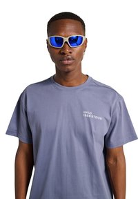 Niebieska bawełniana koszulka z krótkim rękawem z napisem "HALO 196819721981" w białym kolorze na piersi; w połączeniu z białymi sportowymi okularami przeciwsłonecznymi.
