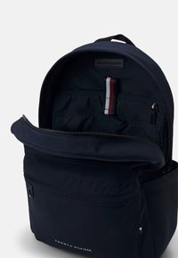 Zaino blu navy con una texture morbida, chiusura con zip, scomparti interni e un piccolo logo. Presenta un accento in tessuto a righe all'interno.