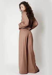 Brązowy, teksturowany strój z zebranym tyłem, długimi rękawami i szerokimi spodniami. Kolor jest ciepły i stonowany, z czystymi liniami.