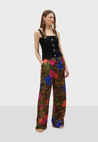 Zwart textuur tanktop met vierkante halslijn en gouden knopen, gecombineerd met wijde broeken met een kleurrijk bloemen- en luipaardprintdesign.