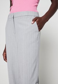 Jasnoszare spodnie w cienkie prążki o prostym kroju, wyposażone w boczne kieszenie i gładką fakturę. Pas przedni płaski z zapięciem na zamek.